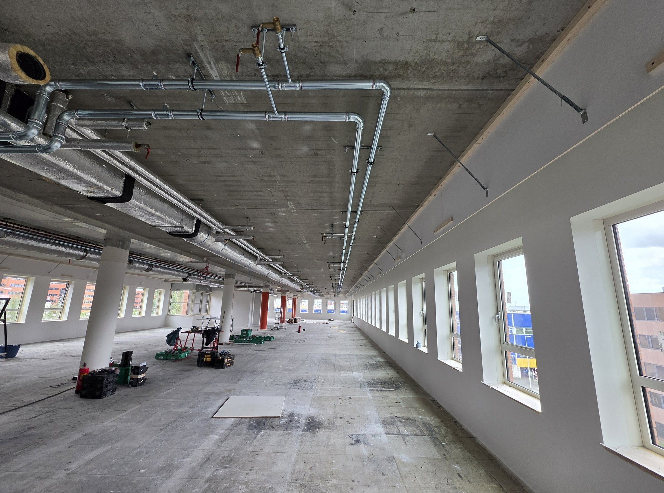 Installatiewerk op een kantoorverdieping in aanbouw, met leidingwerk langs het plafond